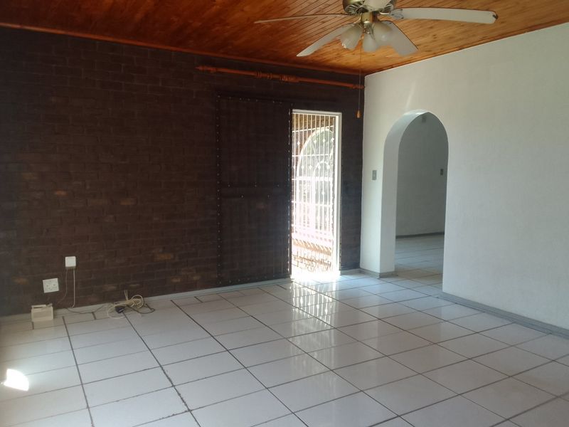 Spacious living area featuring exposed brickwork, timber ceiling, and tiled flooring, leading through an arched doorway to adjacent rooms.