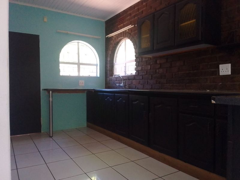 Kitchen featuring dark built-in cabinetry, laminate countertops, stainless steel sink, tiled flooring, and distinctive exposed brick walls with arched windows.