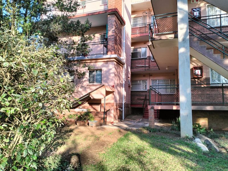 Rear view of a multi-story brick apartment building featuring external metal staircases, balcony access, and communal garden space.