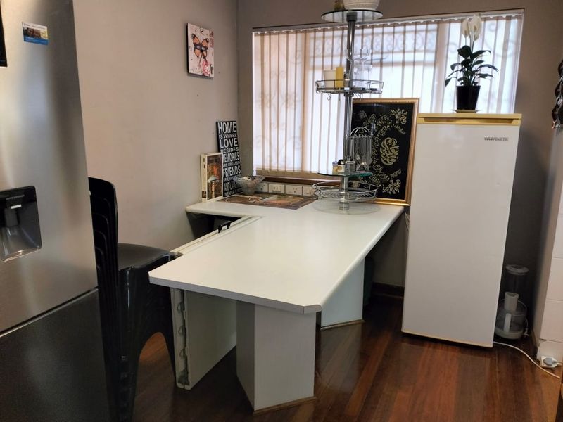 A functional kitchen corner featuring a laminate workspace, timber flooring, and vertical blinds, providing a practical area for food preparation or casual dining.