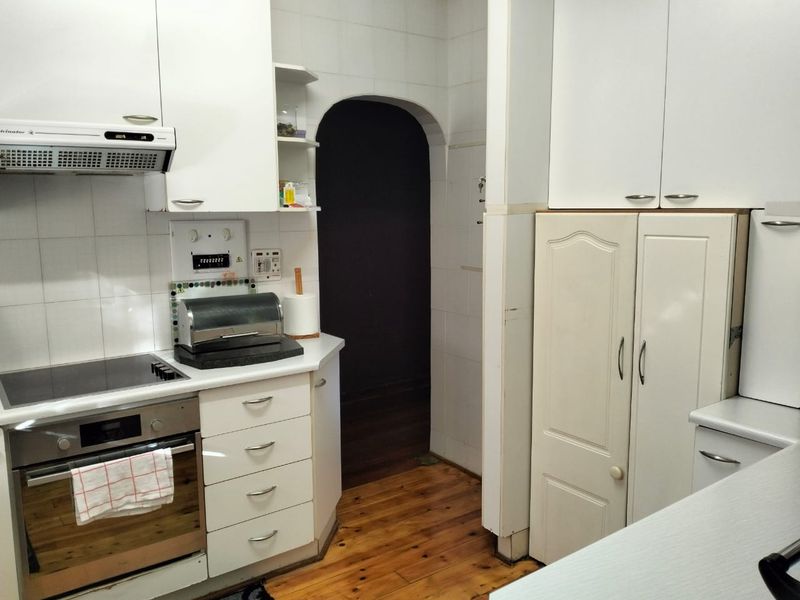 A functional kitchen featuring white built-in cabinetry, an integrated oven and hob, tiled splashbacks, and warm timber flooring with an arched transition to another room.