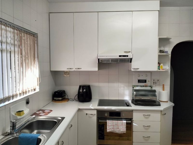 A functional kitchen featuring white cabinetry, a stainless steel sink, an integrated electric hob, and an oven with an overhead extractor fan.