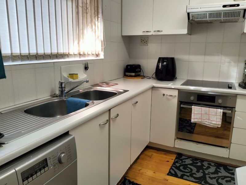 Functional kitchen featuring white cabinetry, built-in oven, electric hob, extractor fan, and a double stainless steel sink with tiled splashbacks.