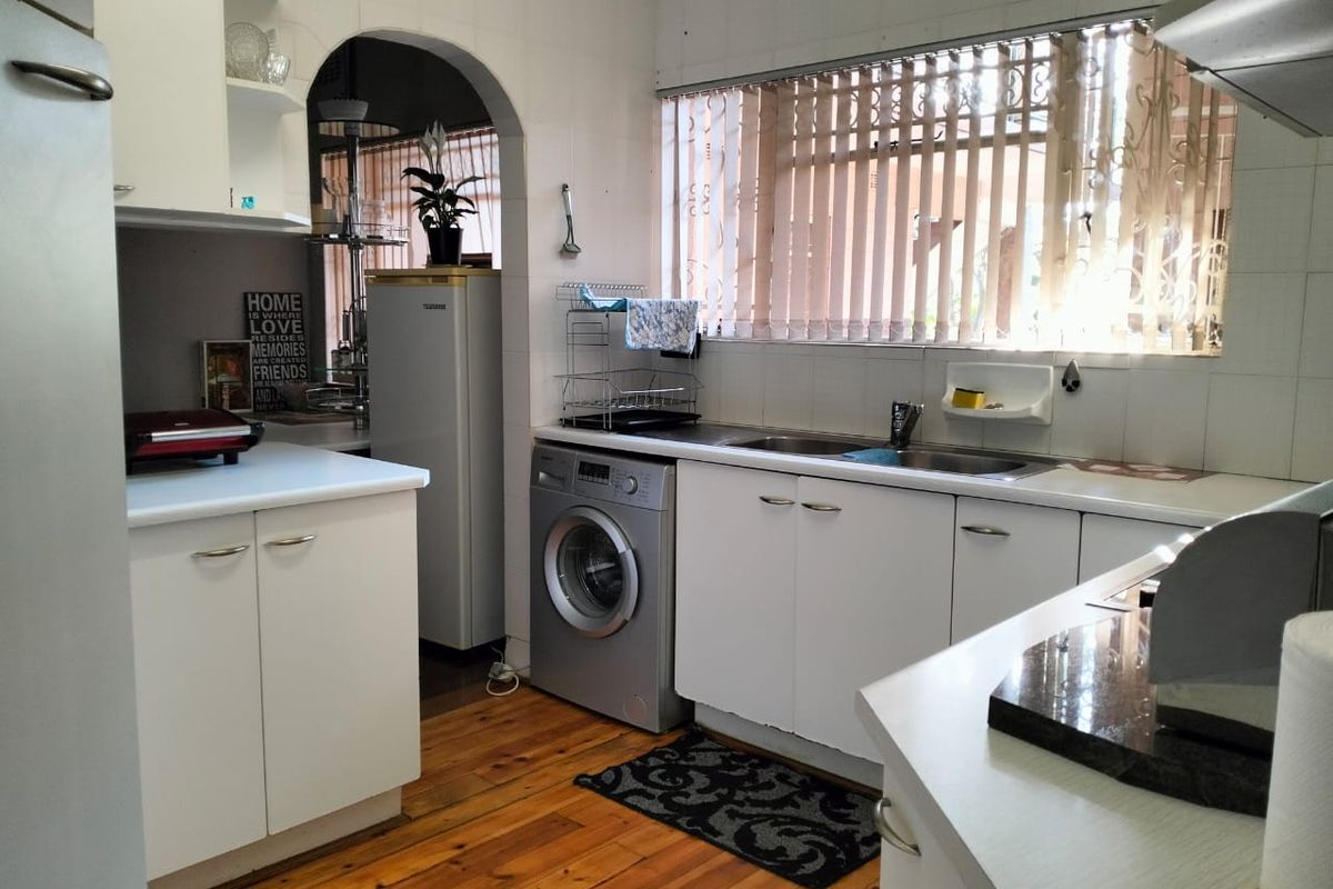 A functional kitchen featuring white built-in cabinetry, laminate countertops, a double basin sink, and timber flooring, with an arched opening to an adjacent space.