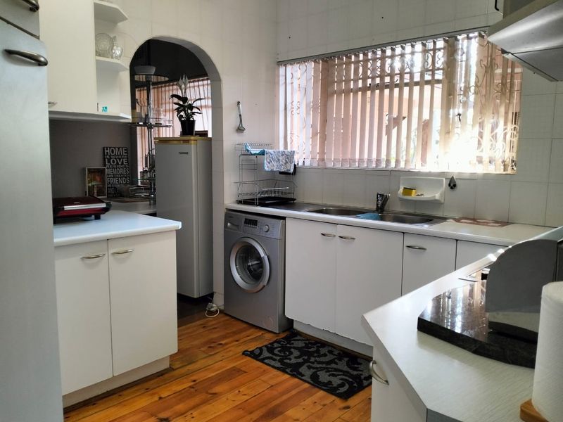 A functional kitchen featuring white built-in cabinetry, laminate countertops, a double basin sink, and timber flooring, with an arched opening to an adjacent space.