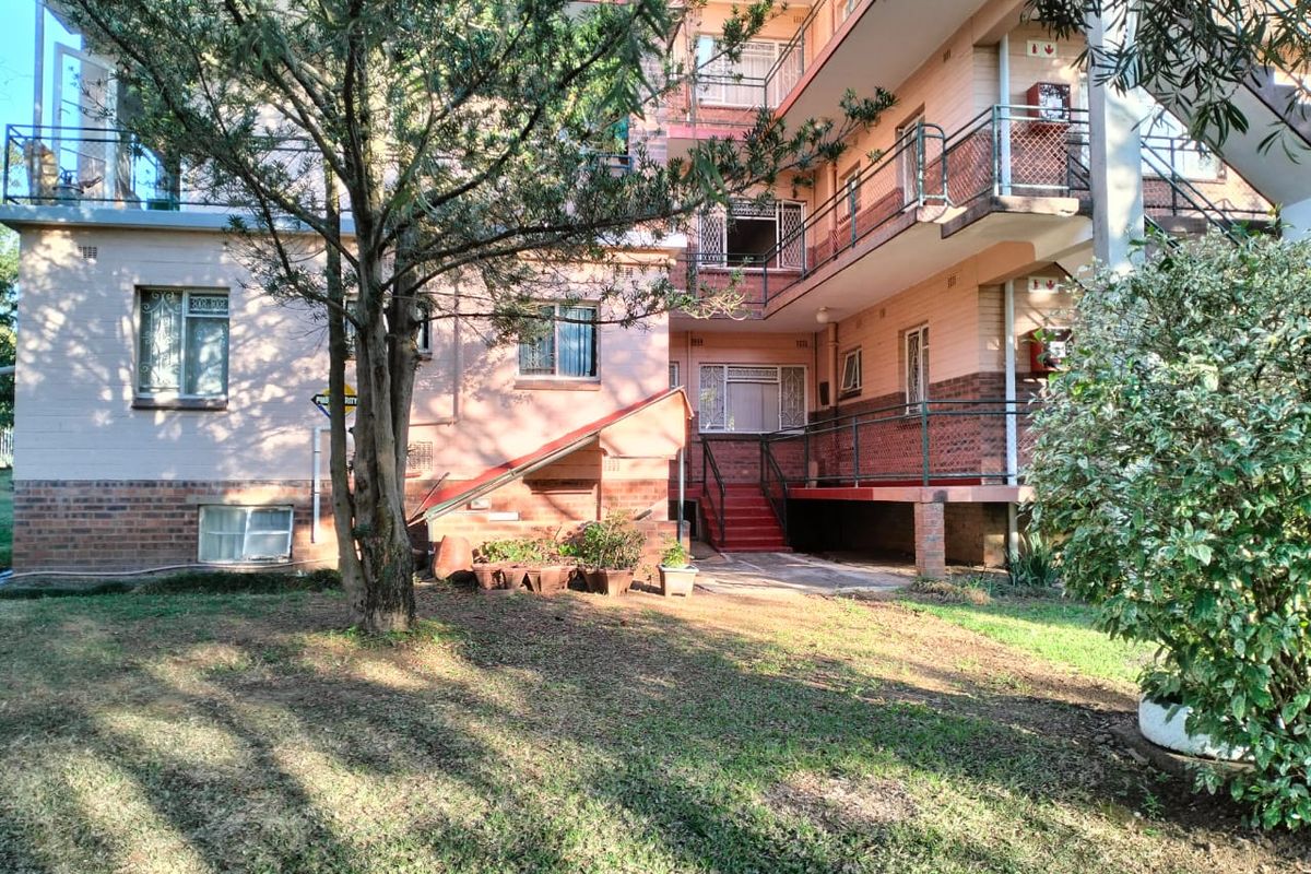 Rear view of a multi-story flat complex featuring brick facade, external staircases, and balcony access with security gates.