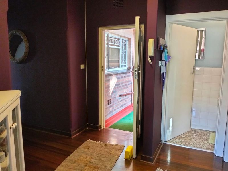 A hallway featuring timber flooring and an intercom system, providing access to an external balcony area and an adjacent room.