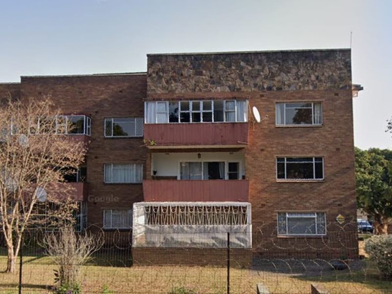 Front elevation of a multi-story brick apartment building featuring stone cladding accents, private balconies, and secure perimeter fencing.