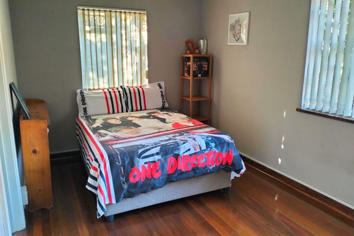 A bedroom featuring polished hardwood flooring, neutral wall tones, and dual windows fitted with vertical blinds.