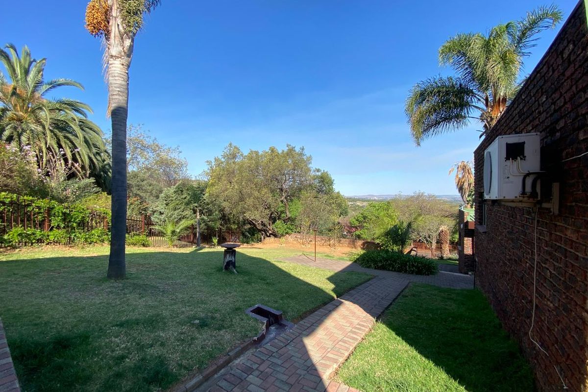 A spacious rear garden featuring a brick paved pathway, established palm trees, and a brick exterior wall with an integrated air conditioning unit.