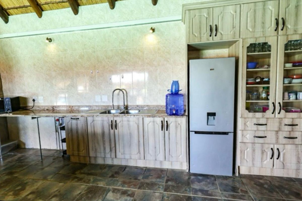 A functional kitchen featuring wood-look cabinetry, granite-style countertops, a double sink, and a high-pitched thatched ceiling with exposed timber beams.