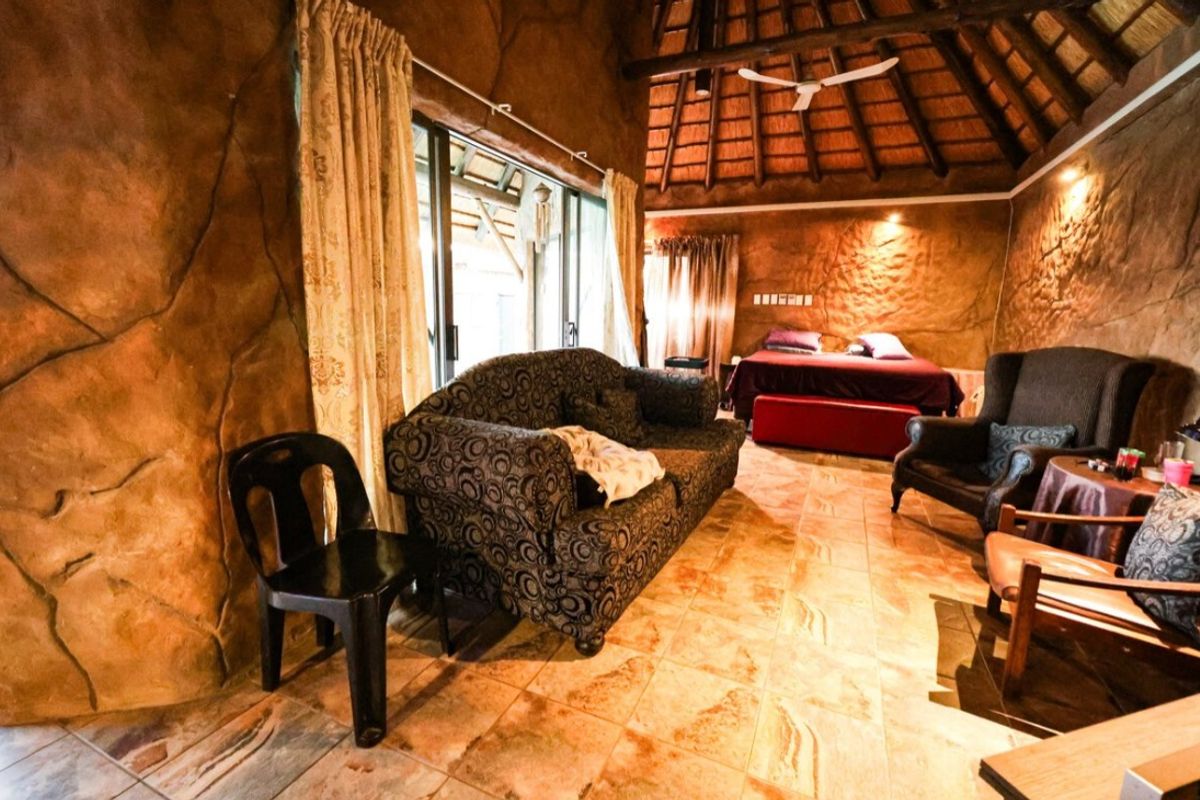 Spacious bedroom featuring a unique textured rock-style wall finish, high thatched ceiling with exposed beams, and tiled flooring with direct access to the patio.