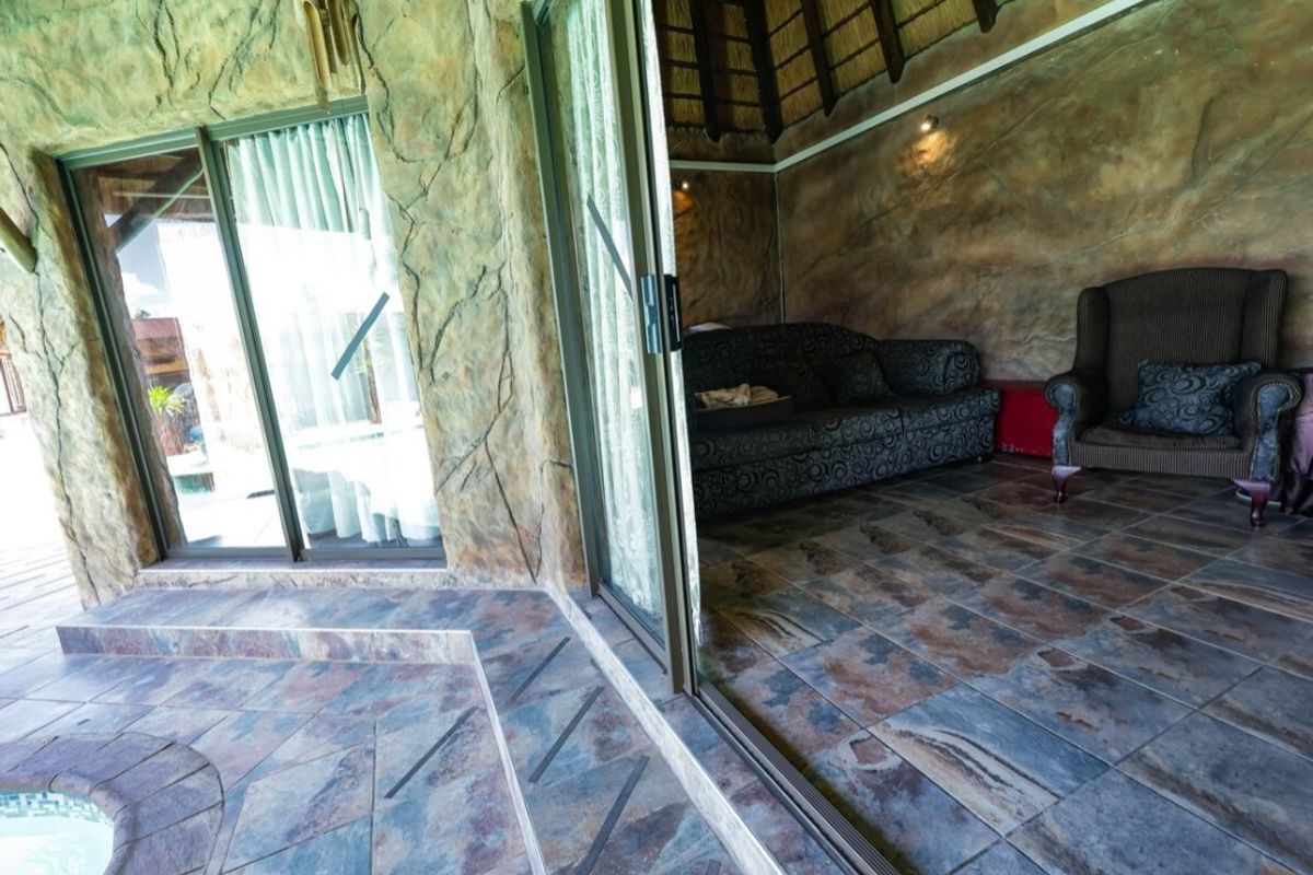 An indoor living area featuring textured rock-effect walls, slate tile flooring, and large sliding glass doors opening onto a pool deck.