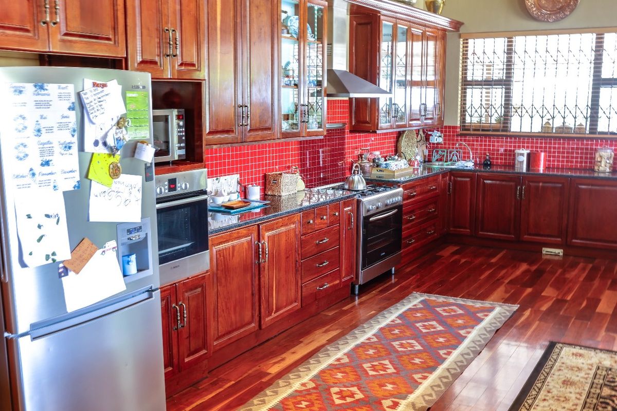 A traditional kitchen featuring rich wooden cabinetry, granite countertops, a red tiled backsplash, and integrated stainless steel appliances.