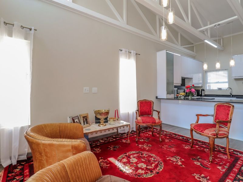 Spacious open-plan living area featuring high vaulted ceilings with exposed trusses, modern kitchen cabinetry, and stone countertops in a bright, well-maintained retirement village unit.