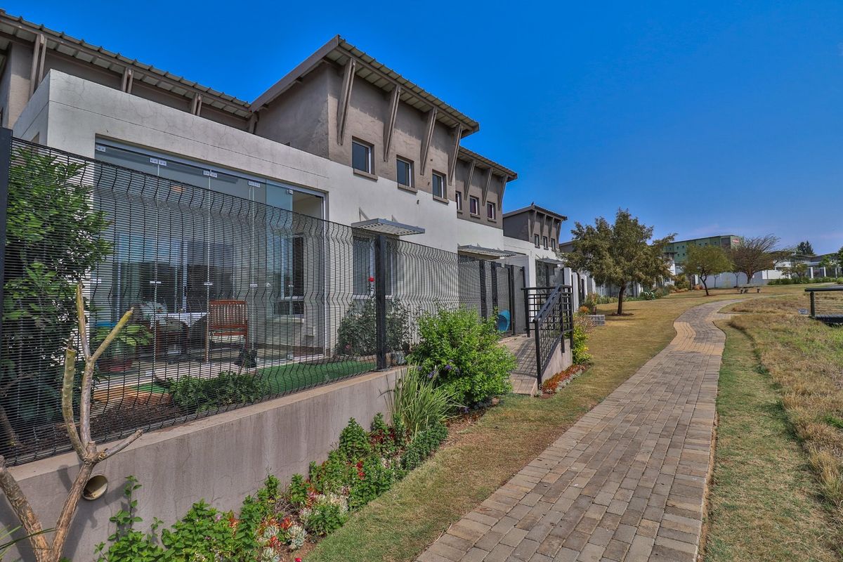 Rear view of the retirement village units featuring paved walkways, landscaped gardens, and modern exterior finishes with glass sliding doors.