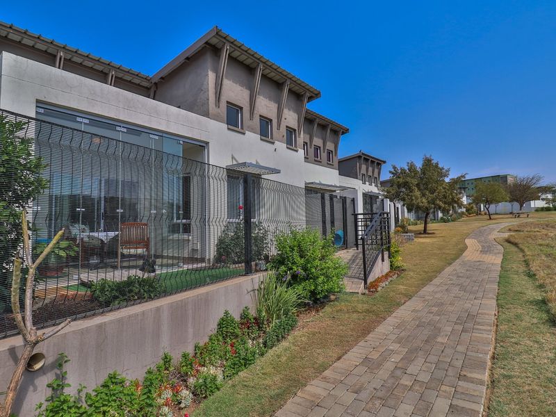 Rear view of the retirement village units featuring paved walkways, landscaped gardens, and modern exterior finishes with glass sliding doors.