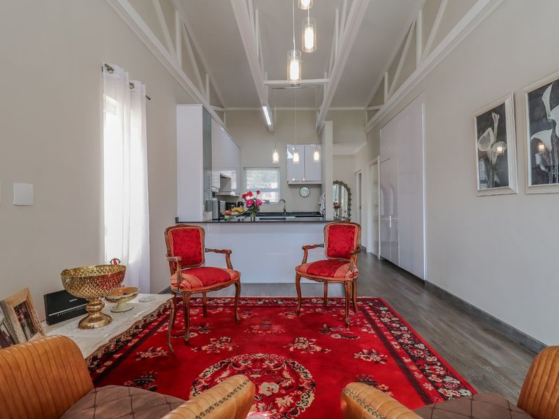 Open-plan living area featuring a modern kitchen with stone benchtops, vaulted ceilings with exposed trusses, and contemporary pendant lighting.