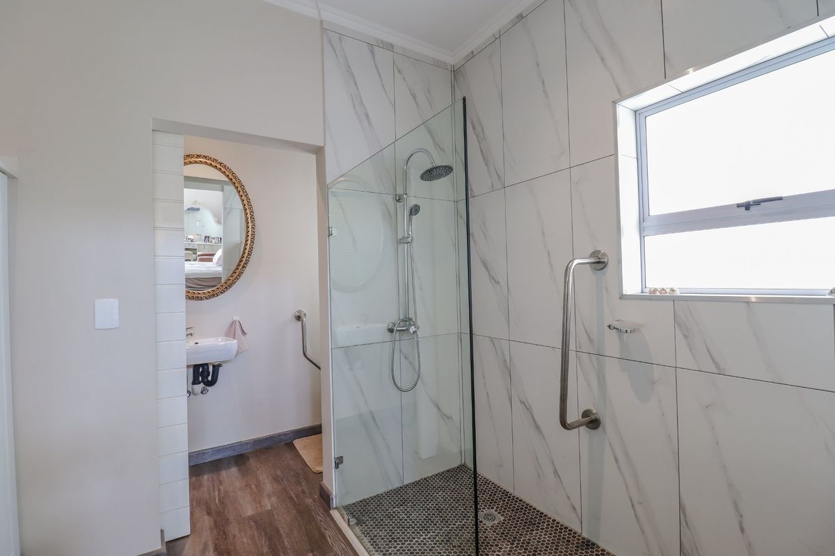 Modern bathroom featuring a walk-in shower with marble-look tiling, glass screen, rain shower head, and safety grab rails for accessibility.