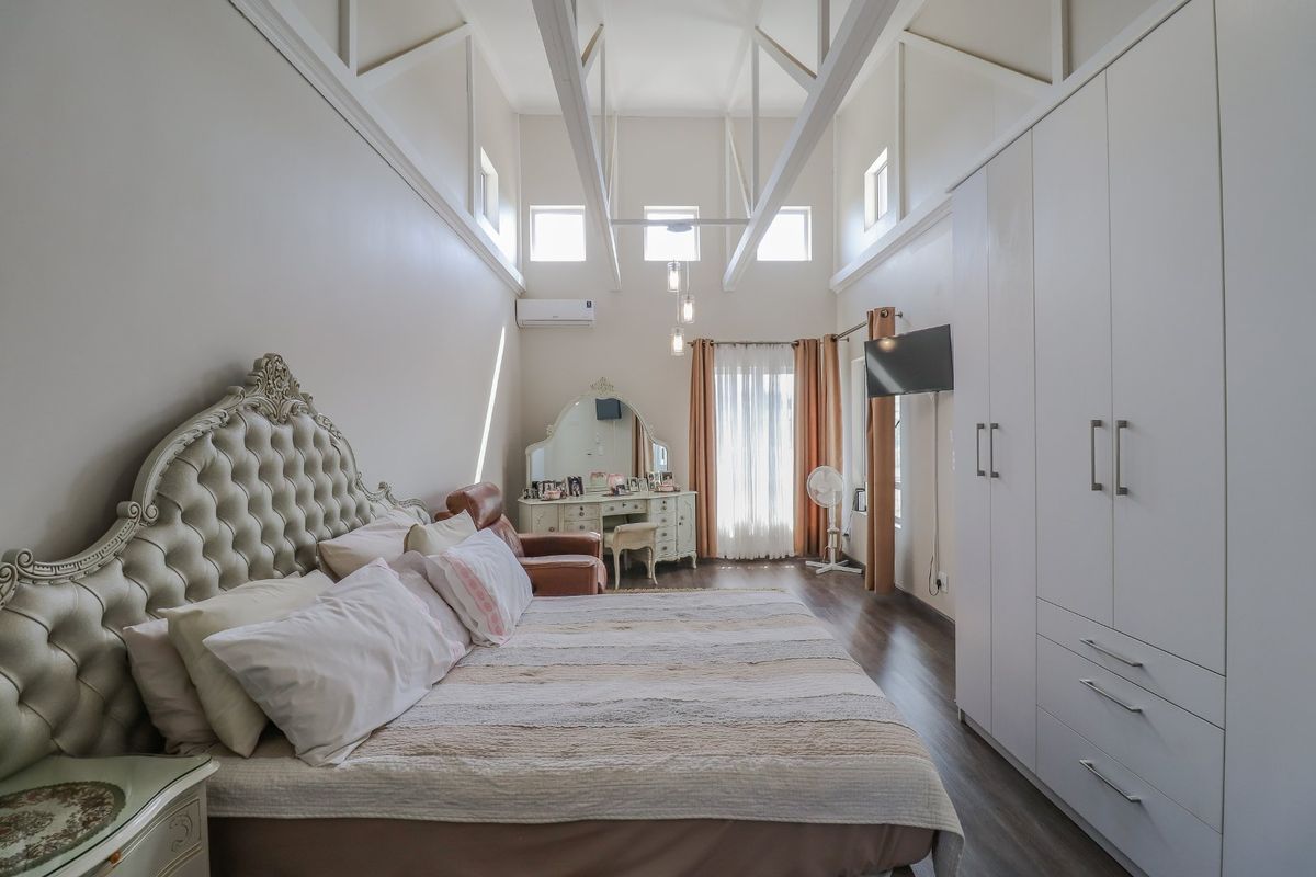 Spacious bedroom featuring high vaulted ceilings with exposed trusses, built-in floor-to-ceiling wardrobes, and modern laminate flooring.