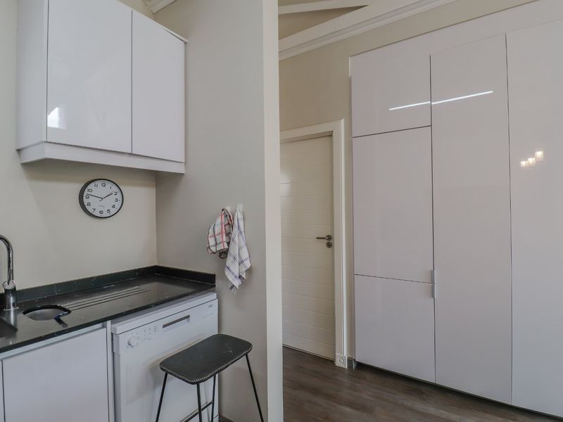 Modern kitchen area featuring sleek white cabinetry, integrated dishwasher, dark stone countertops, and ample storage space with full-height pantry cupboards.