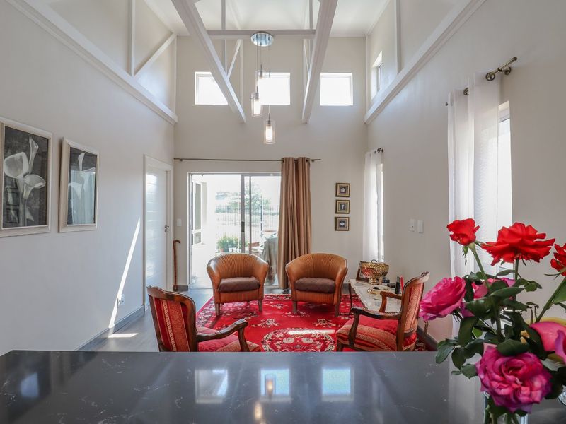 Bright open-plan living area featuring a high vaulted ceiling with exposed rafters, modern pendant lighting, and direct access to an outdoor patio.