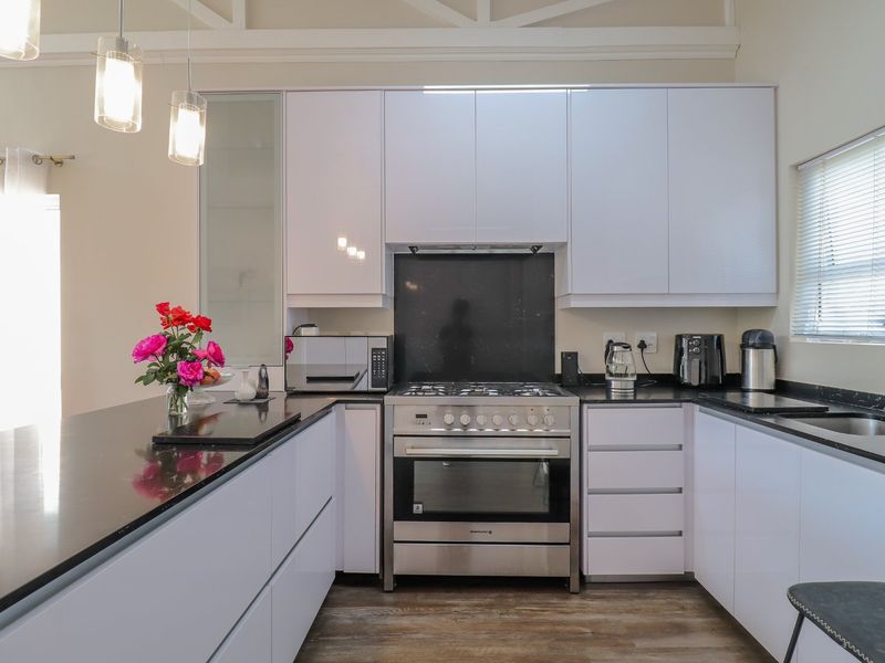 Modern kitchen featuring white cabinetry, black stone countertops, stainless steel gas stove, and oven, complemented by stylish pendant lighting and timber-look flooring.