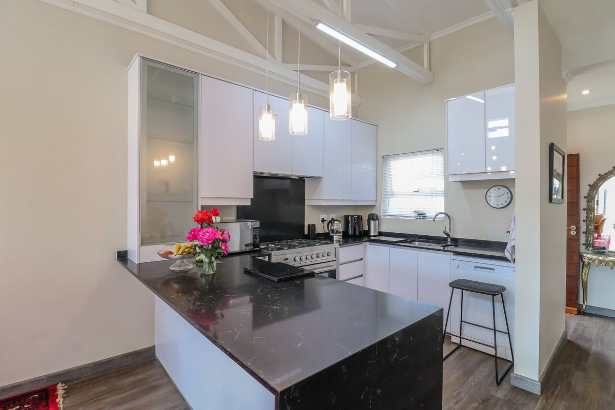 Modern kitchen featuring stone benchtops, white gloss cabinetry, gas cooktop, and exposed ceiling trusses, creating a bright and functional culinary space.