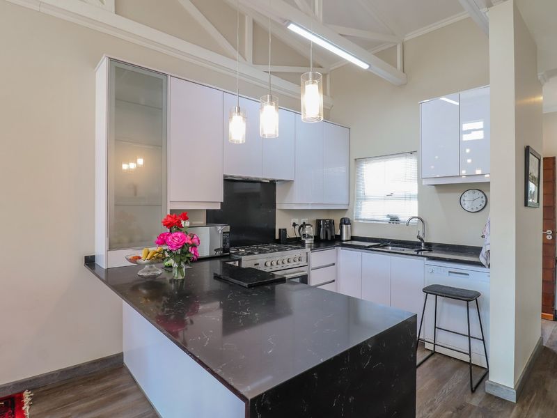 Modern kitchen featuring stone benchtops, white gloss cabinetry, gas cooktop, and exposed ceiling trusses, creating a bright and functional culinary space.