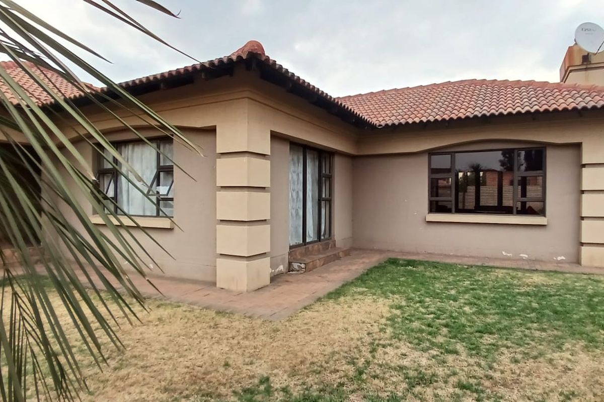 Rear view of a single-story house featuring a tiled roof, paved walkway, and established garden area.