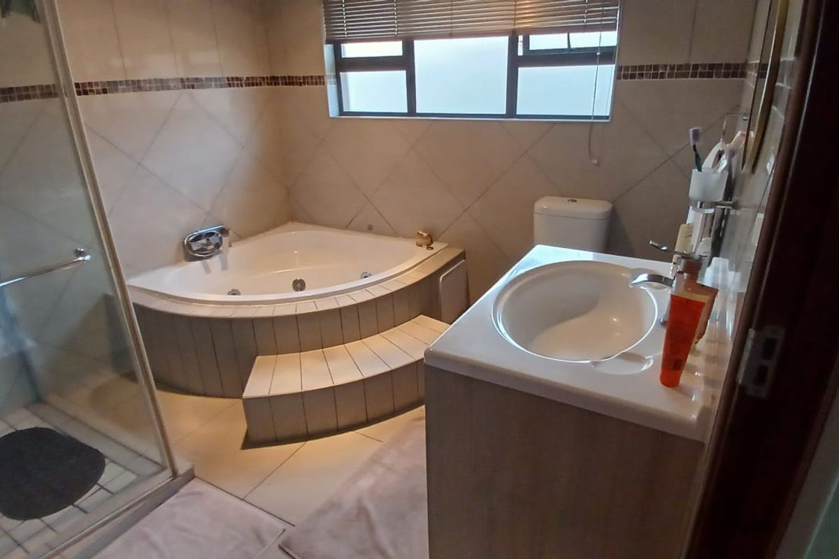 A functional bathroom featuring a corner spa bath with tiled steps, a separate glass-enclosed shower, and a vanity basin.