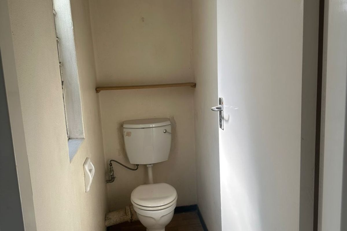 A compact, functional guest toilet featuring a standard white toilet suite and wood-look flooring.