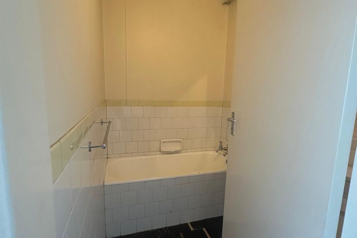 A compact bathroom featuring a built-in bathtub with tiled surround, wall-mounted towel rail, and dark patterned flooring.