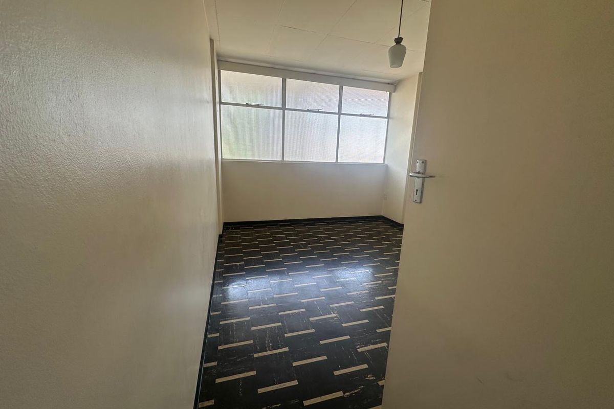 An empty bedroom featuring large windows, a pendant light fixture, and patterned floor tiles, offering a blank canvas for renovation.