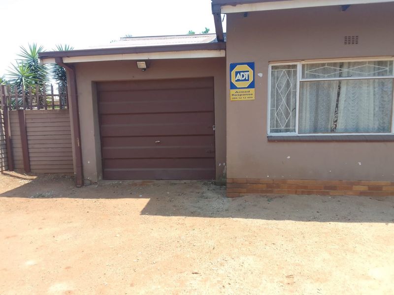 Front exterior view of the property featuring a single garage door, security alarm signage, and a metal-framed window.