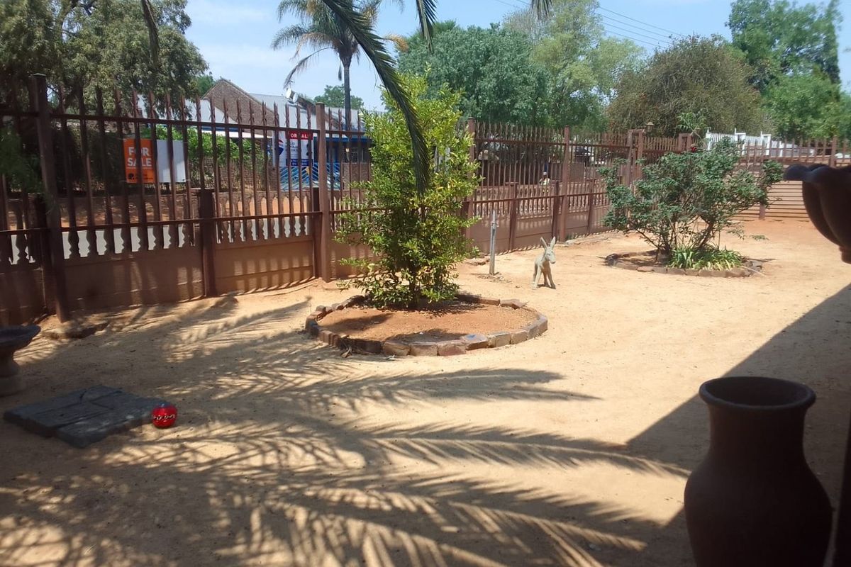 A rear garden area featuring metal perimeter fencing and a central landscaped garden bed with established trees.