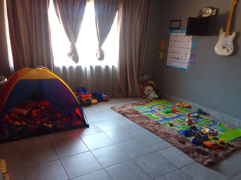 A bedroom featuring neutral grey walls and tiled flooring, currently utilized as a children's play area with natural light from the window.