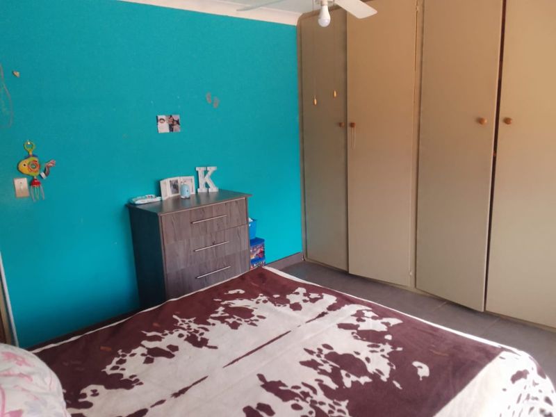 A bedroom featuring built-in cupboards and a ceiling fan, currently finished with a vibrant blue accent wall.