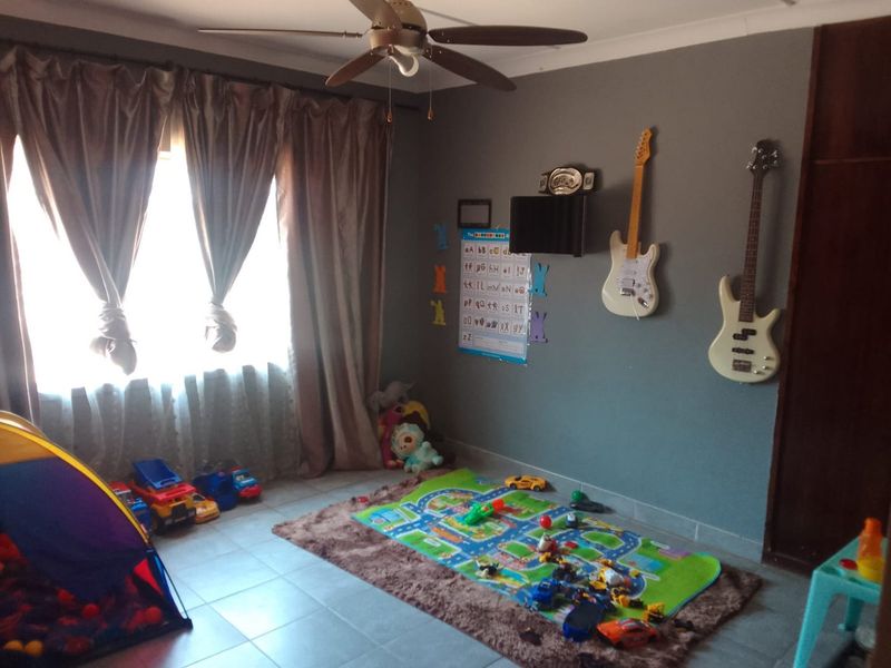A bedroom featuring tiled flooring, a ceiling fan, and a built-in cupboard, currently utilized as a children's play area.
