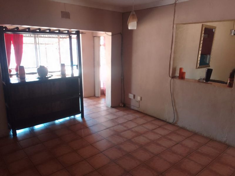 An empty living room featuring tiled flooring and a built-in serving hatch, offering a functional layout ready for renovation and personalization.