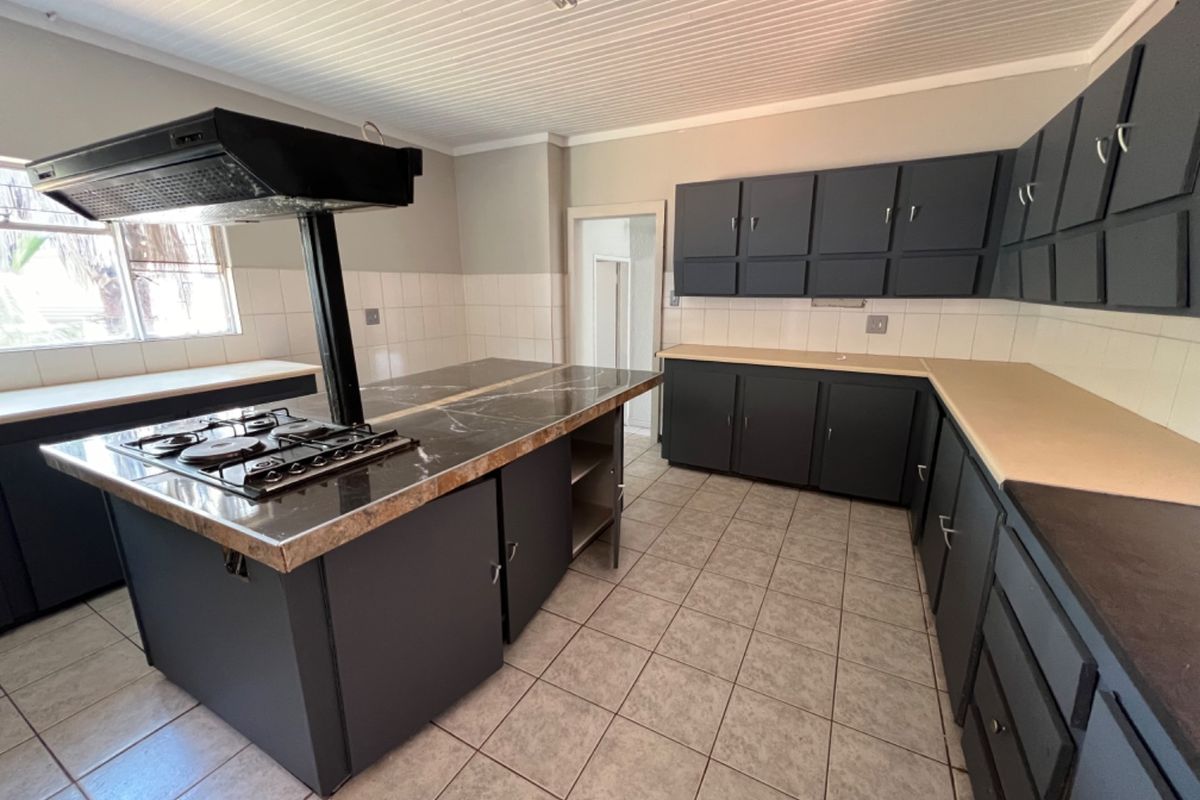 Spacious kitchen featuring a central island with a built-in gas hob and extractor fan, ample dark cabinetry, and tiled flooring.