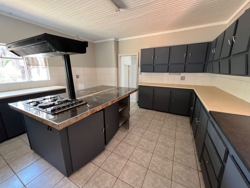 Spacious kitchen featuring a central island with a built-in gas hob and extractor fan, ample dark cabinetry, and tiled flooring.