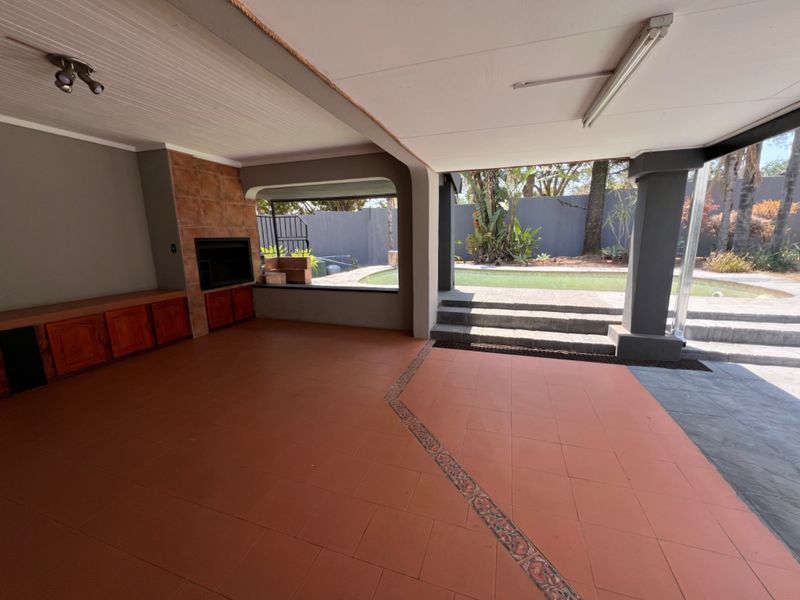 Covered patio area featuring a built-in fireplace, tiled flooring, and direct access to the swimming pool and garden.