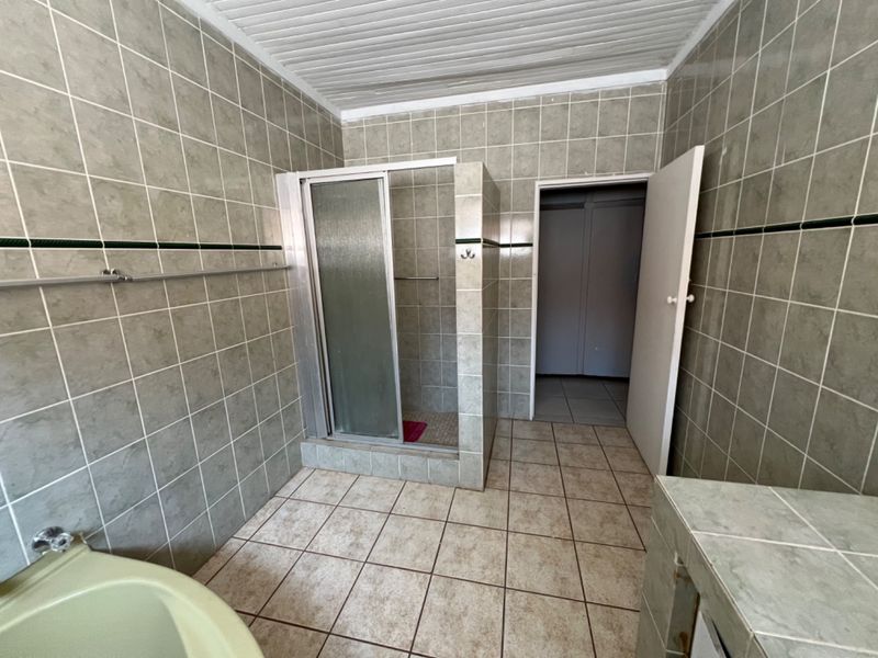 A dated bathroom featuring full-height wall tiling, a built-in shower enclosure, and tiled flooring, offering a functional space ready for modernization.