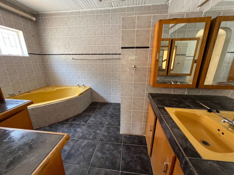 A dated bathroom featuring a yellow built-in bathtub and matching vanity sink, complemented by dark tiled flooring and wall tiling.