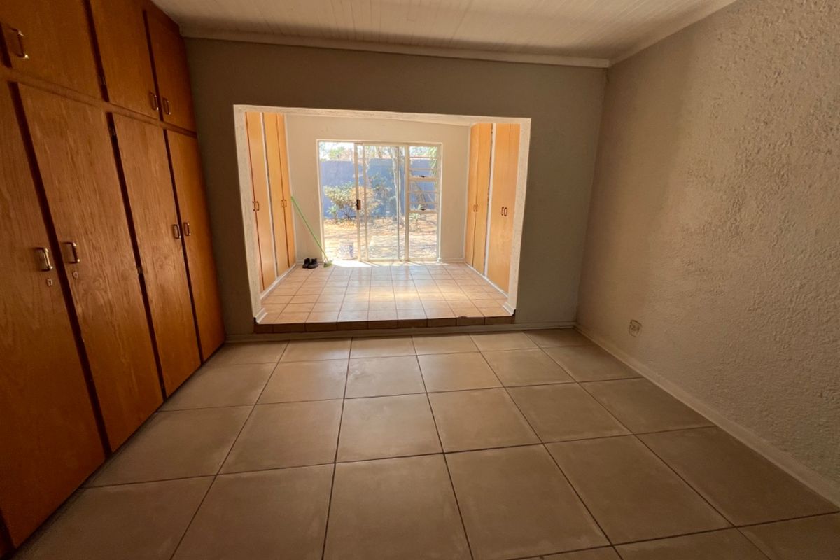 A vacant bedroom featuring built-in wooden cupboards and a raised sunroom area with sliding glass doors leading to the rear garden.