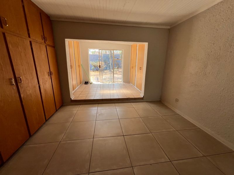 A vacant bedroom featuring built-in wooden cupboards and a raised sunroom area with sliding glass doors leading to the rear garden.