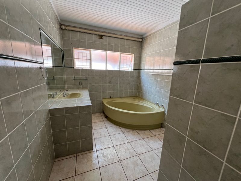 A dated bathroom featuring a corner bathtub, built-in vanity with integrated basin, and full-height wall tiling.