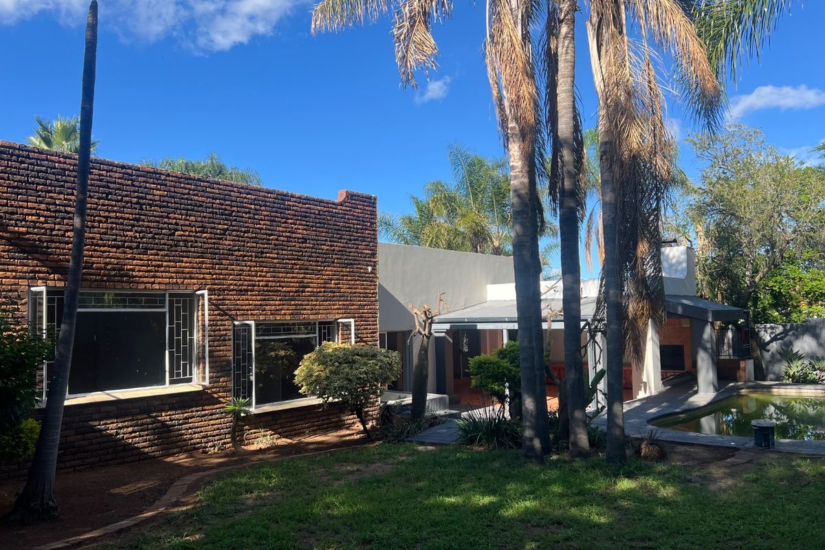 Rear view of the property featuring a brick facade, covered patio area, and a swimming pool set within a landscaped garden.