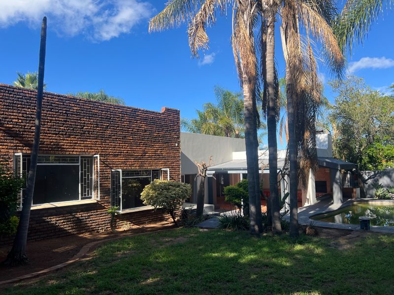 Rear view of the property featuring a brick facade, covered patio area, and a swimming pool set within a landscaped garden.